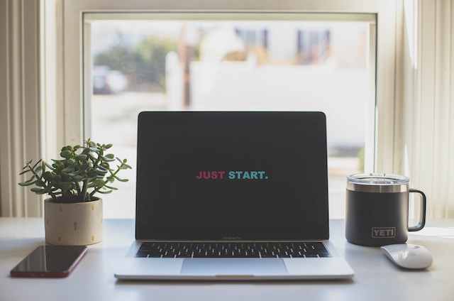 机に置かれたノートパソコン画面に「JUST START」の文字が表示されている